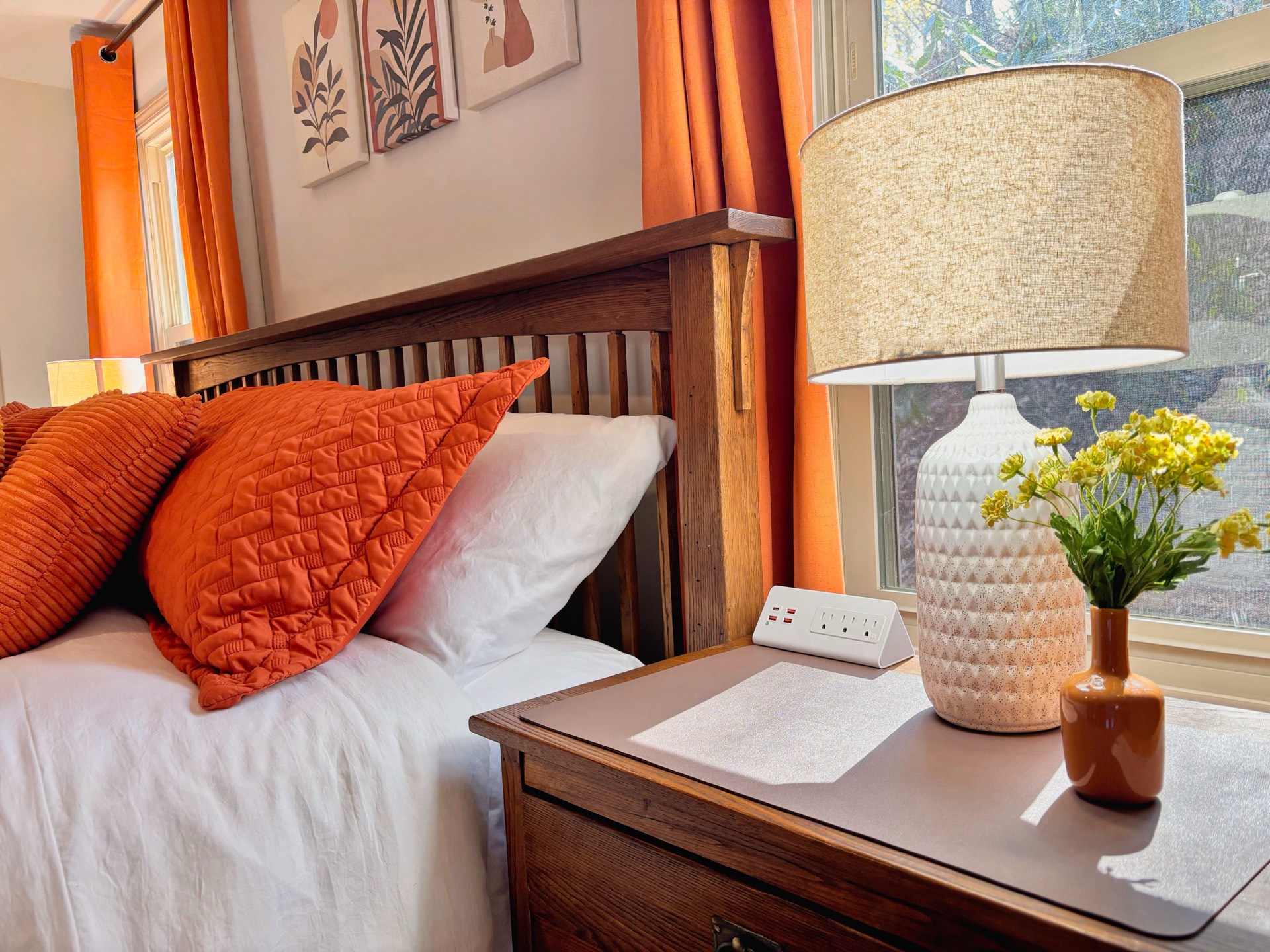 Bedside detail with orange pillows, lamp, and fresh flowers